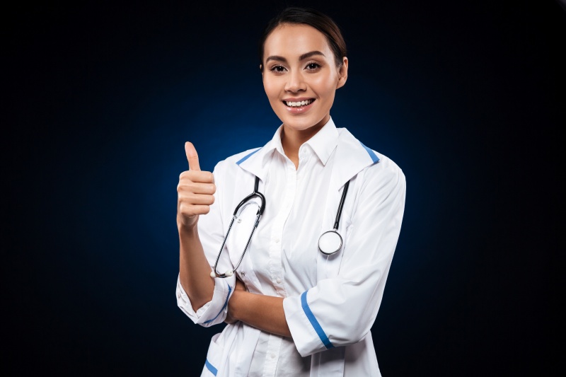 Young positive woman doctor with stethoscope showing thumb up